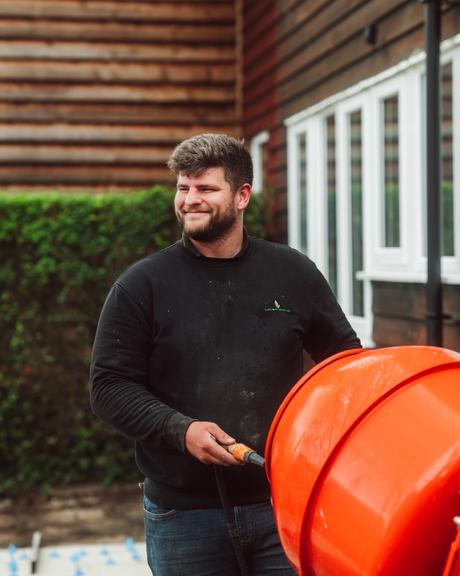 Landscaper smiling while hosing down an orange cement mixer