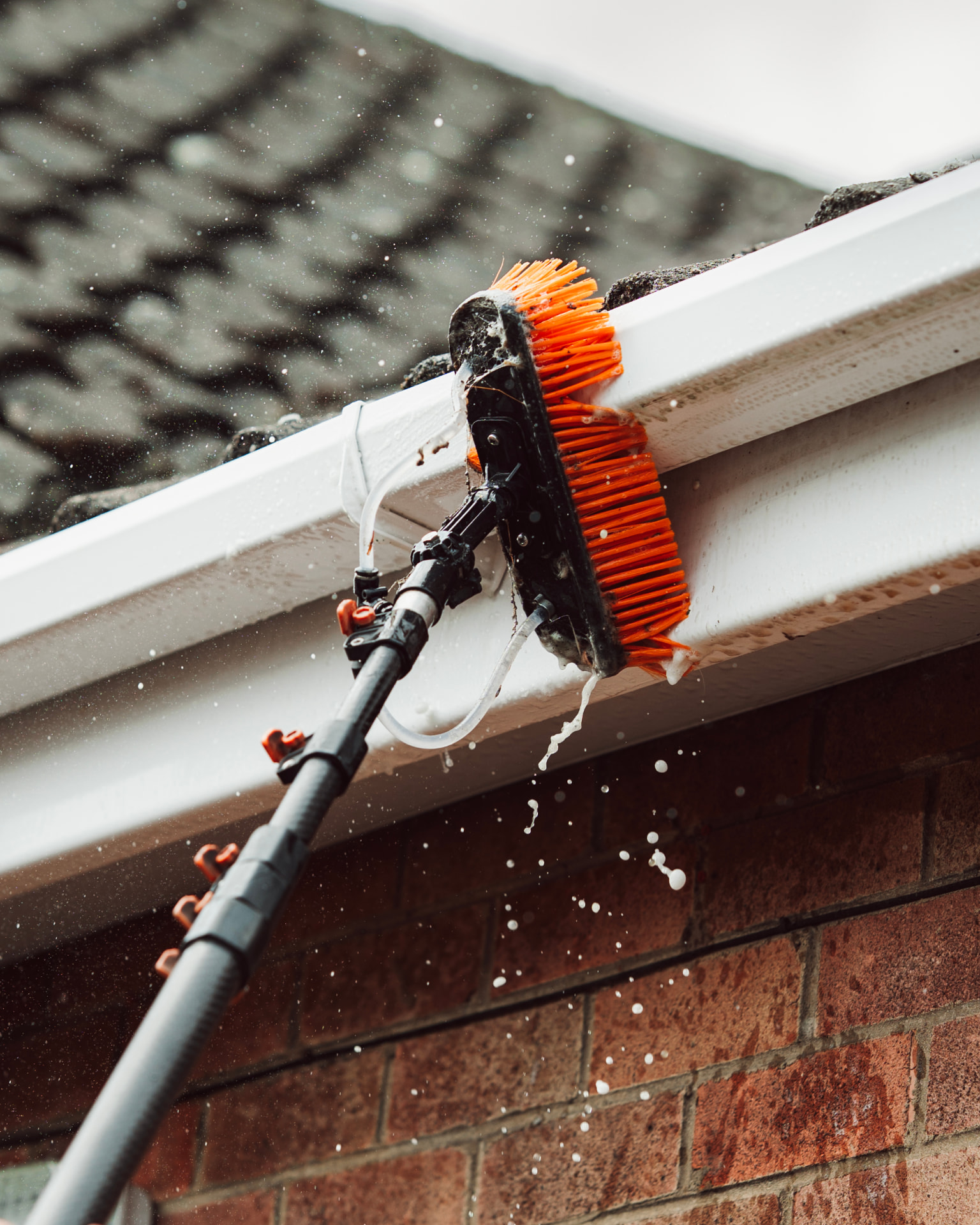 Gutter brush cleaning a white gutter on a brick house